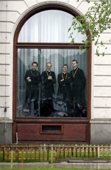 Four priests stand in an office window to watch the Pope's Mass in Warsaw.